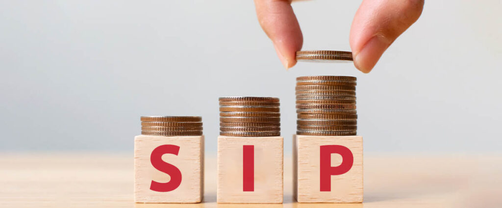 Image of a hand picking coins with three individual heaps of coins below. The top of the image has the text 'SIP', symbolizing the concept of systematic investment and gradual wealth accumulation."
